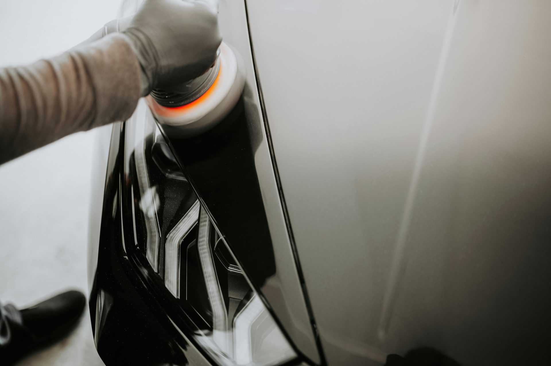 Nahaufnahme einer Person, die ein schwarzes Auto mit einer Poliermaschine poliert.