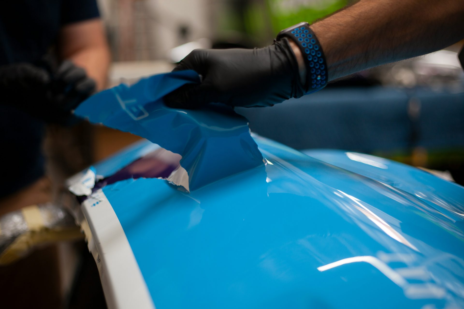 eine Person mit Handschuhen lackiert ein blaues Auto